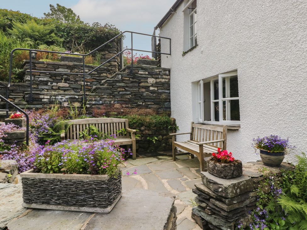 A garden with stone walls and wooden benches at Rose Cottage in Broughton-In-Furness