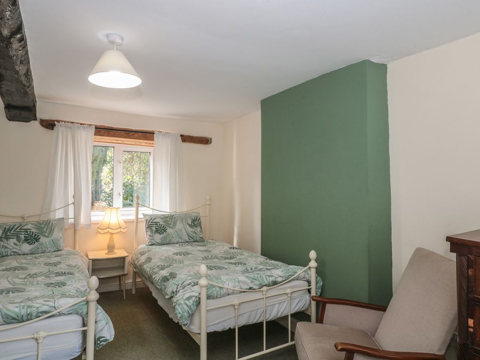 A bedroom with two beds and a chair at 1 Westcroft Cottage in King's Stanley