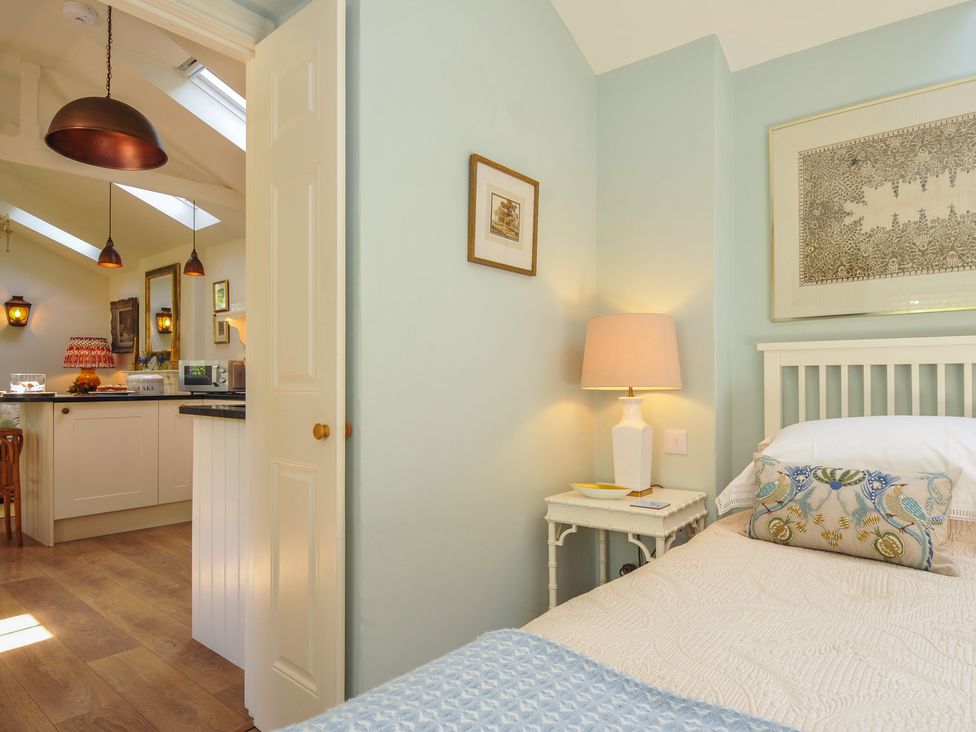 A bedroom with a bed and side table leading to a kitchen at The Coach House at Pendower House Fowey