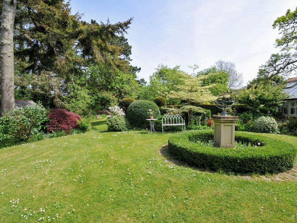 A garden with trees, bushes, and a sundial at The Coach House at Pendower House Fowey