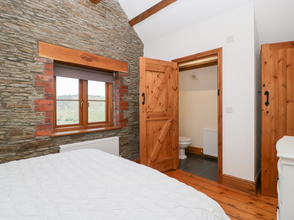 A bedroom with a window and a door leading to a bathroom at Penrhiwarwydd Barn Pontywaun