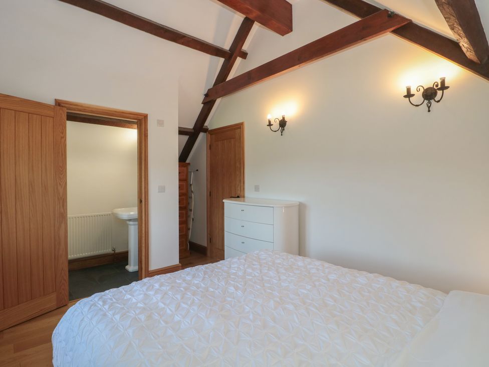A bedroom with a bed, drawers, and an adjoining bathroom at Penrhiwarwydd Barn Pontywaun