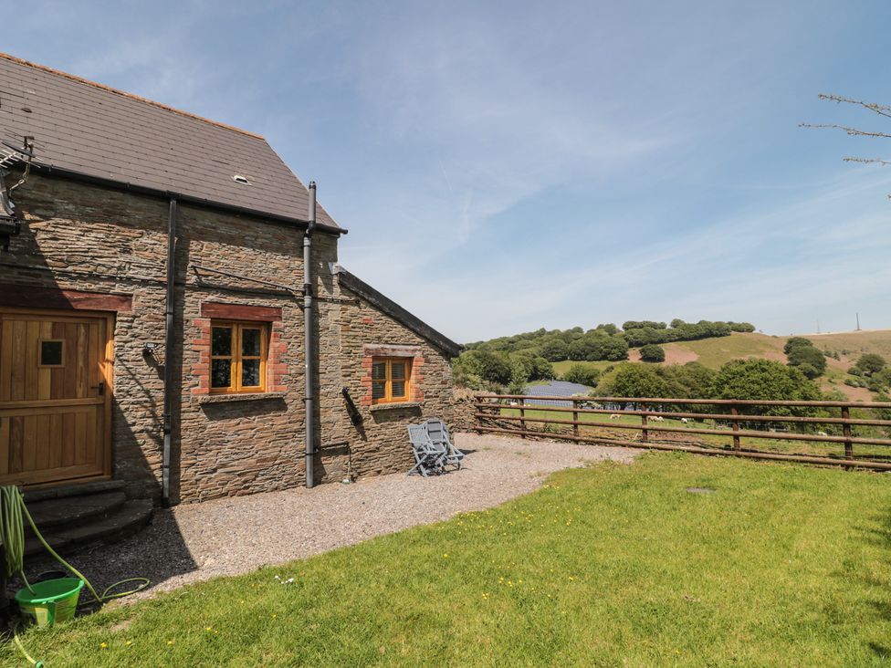 An outdoor area with a stone building and chairs at Penrhiwarwydd Barn Pontywaun
