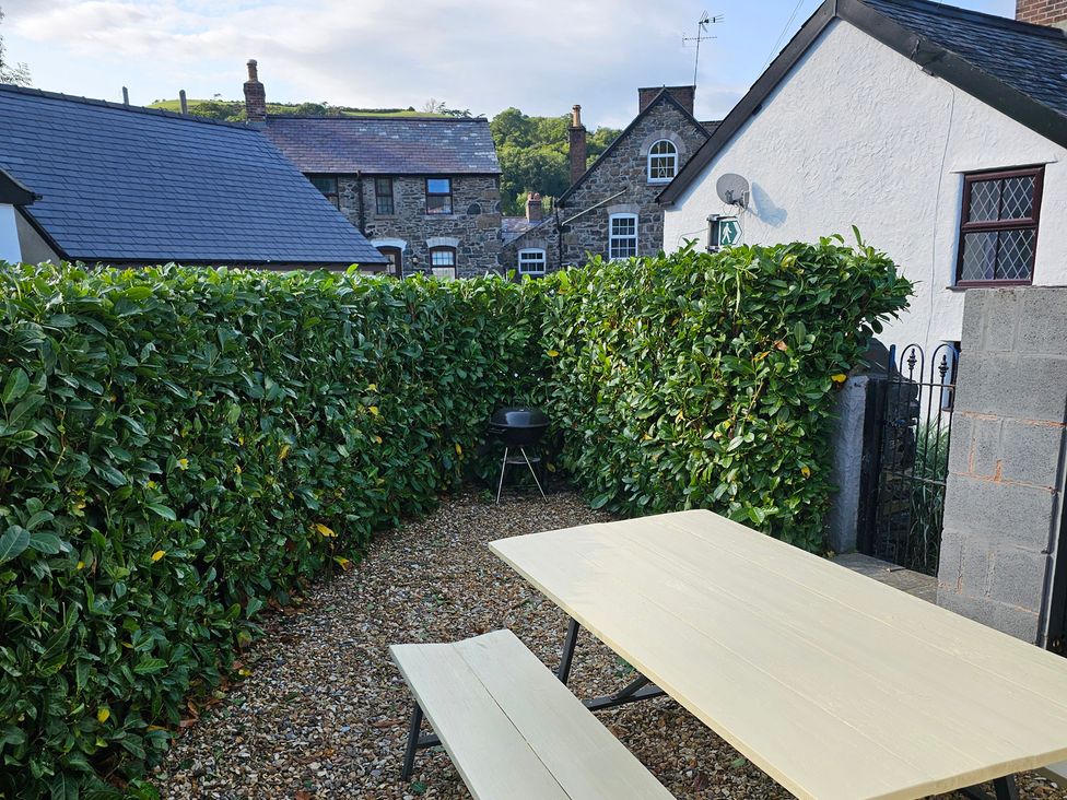 A garden with a table and bench surrounded by a hedge at Dove Cottage Llanfair Talhaiarn