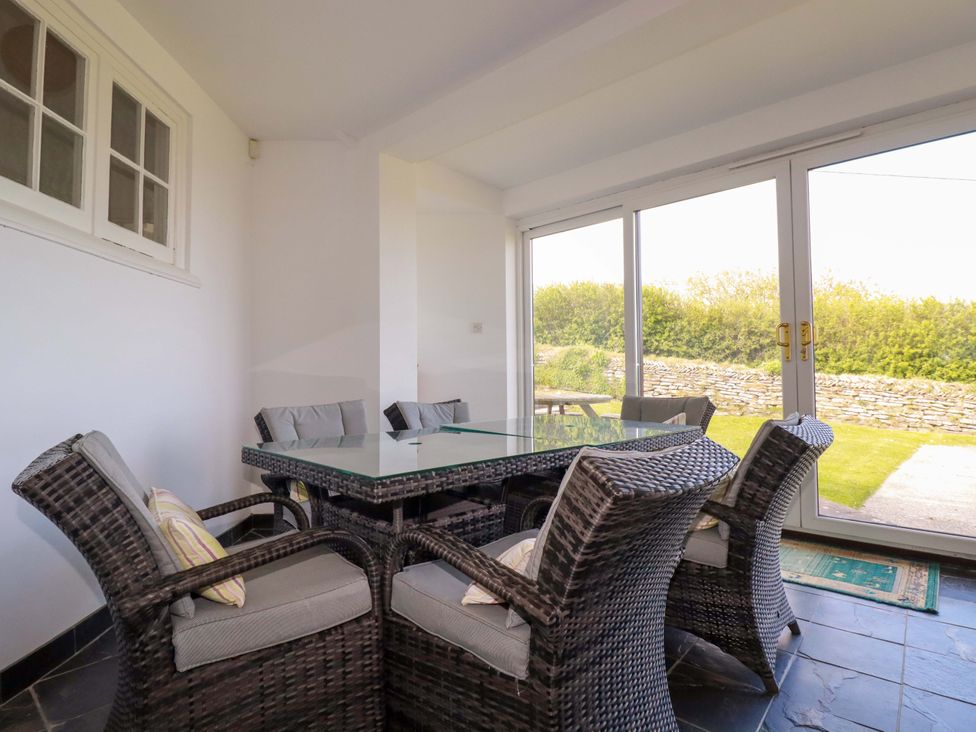 A conservatory with a glass table and wicker chairs at Pentreath in Crantock