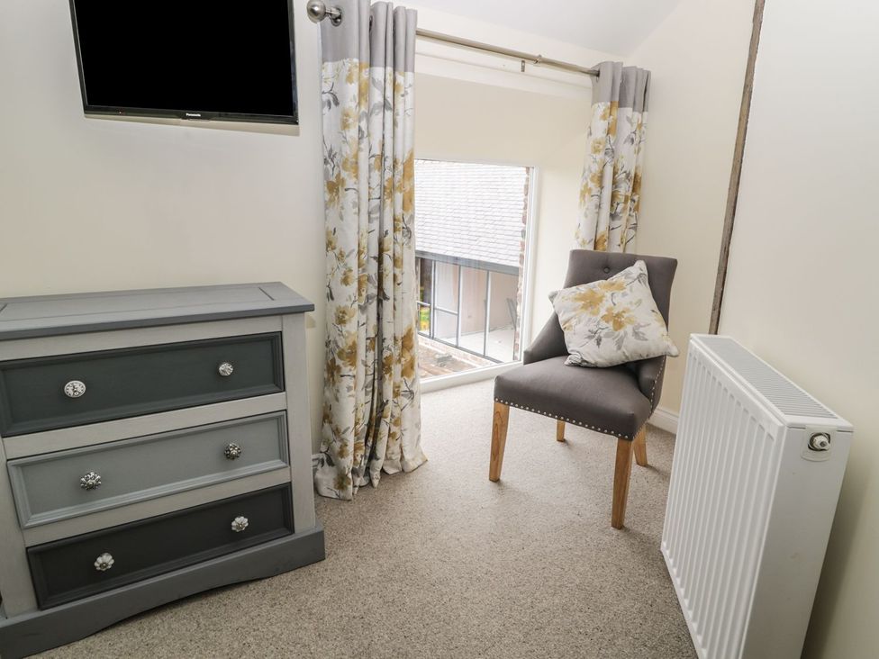 A bedroom with a television, dresser, chair and curtains at The Turnip Barn in 