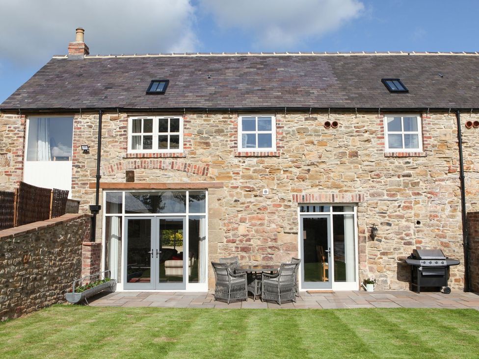 An outdoor area with a stone house, patio furniture, and a barbecue at The Turnip Barn in 