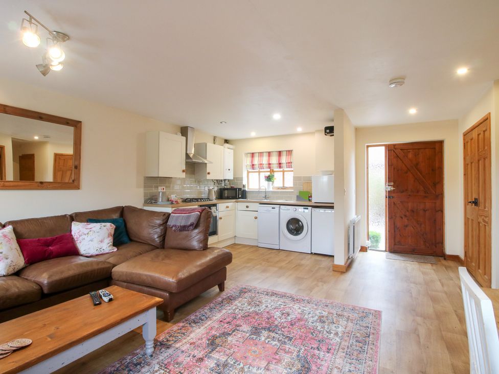 A living room with a sofa and kitchen units at Old Hall Barn 1 Church Stretton