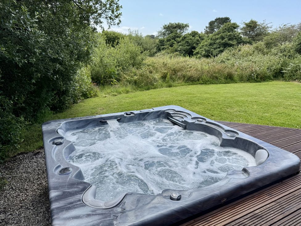 A hot tub on decking in a garden at Willow Lodge in Constantine near Falmouth