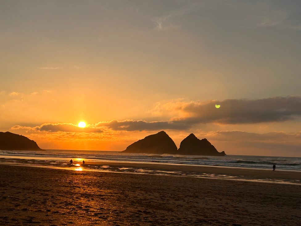 A sunset over the ocean with people on the beach at Holywell Bay View in Holywell Bay