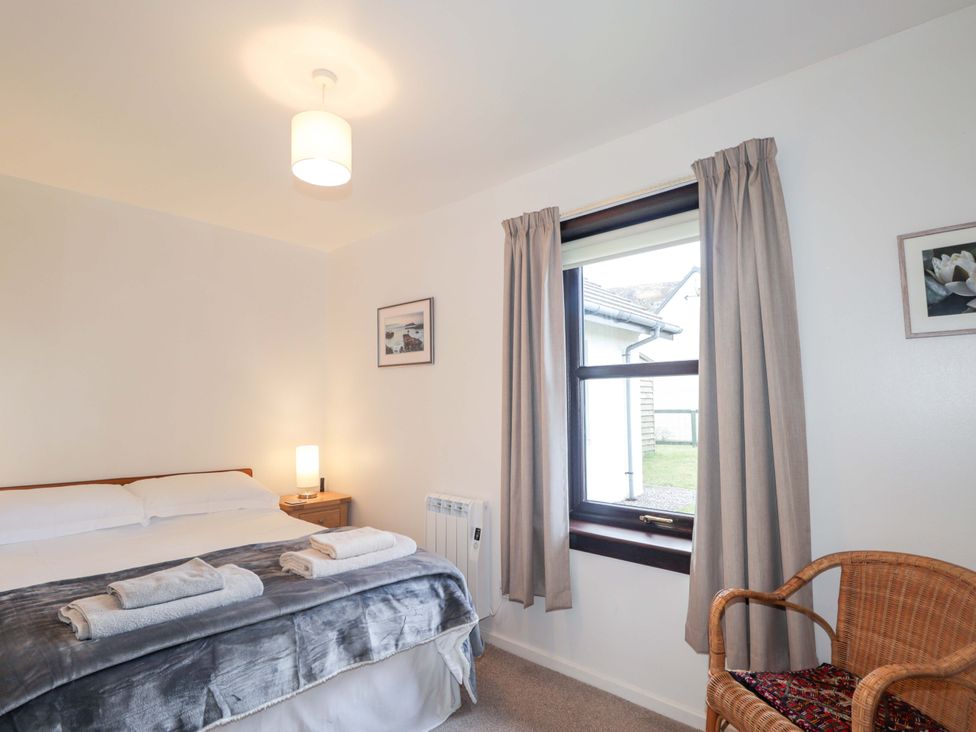 A bedroom with a bed and wicker chair at Church House in Poolewe