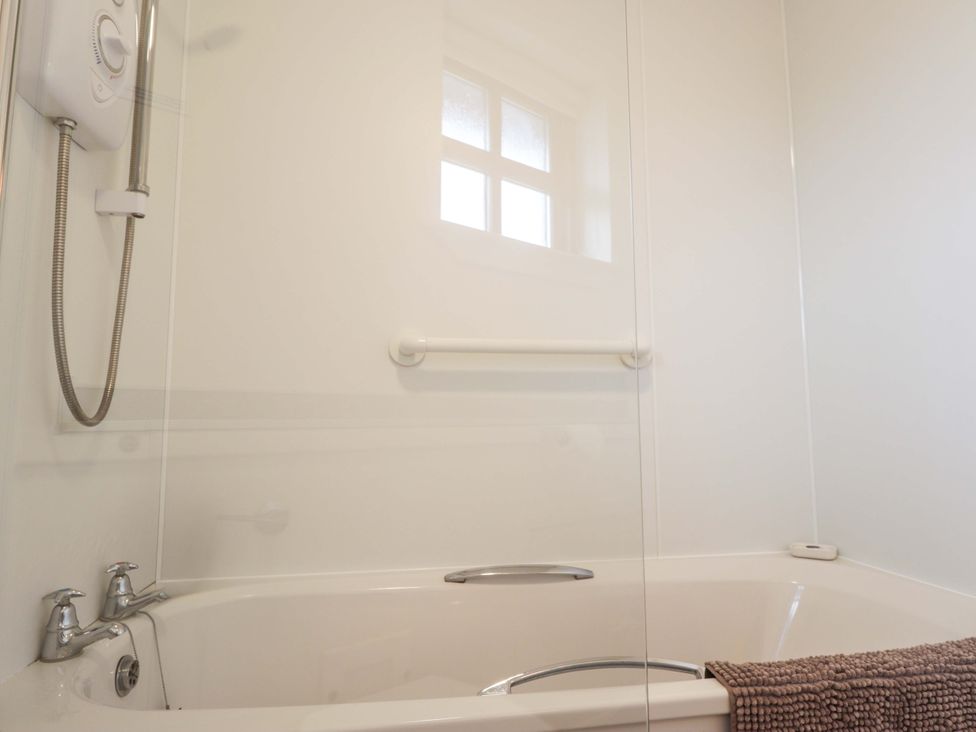 A bathtub with a shower and grab rail at Church House in Poolewe