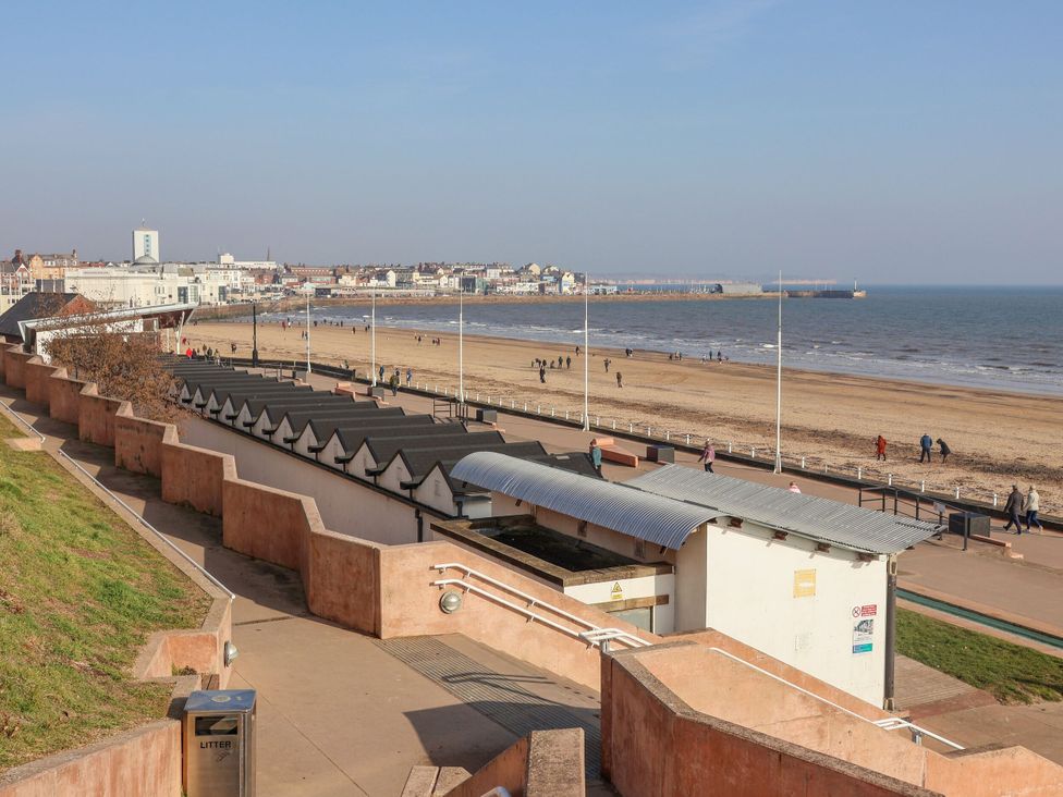 A beach with beach huts and people walking at Apt 5 @ Hunter's Quay, Bridlington