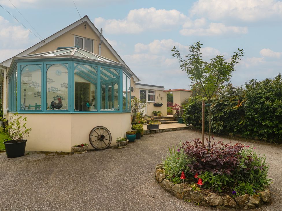 A conservatory next to a house with a flower bed and tree at Woolly Welcome in Goldsithney