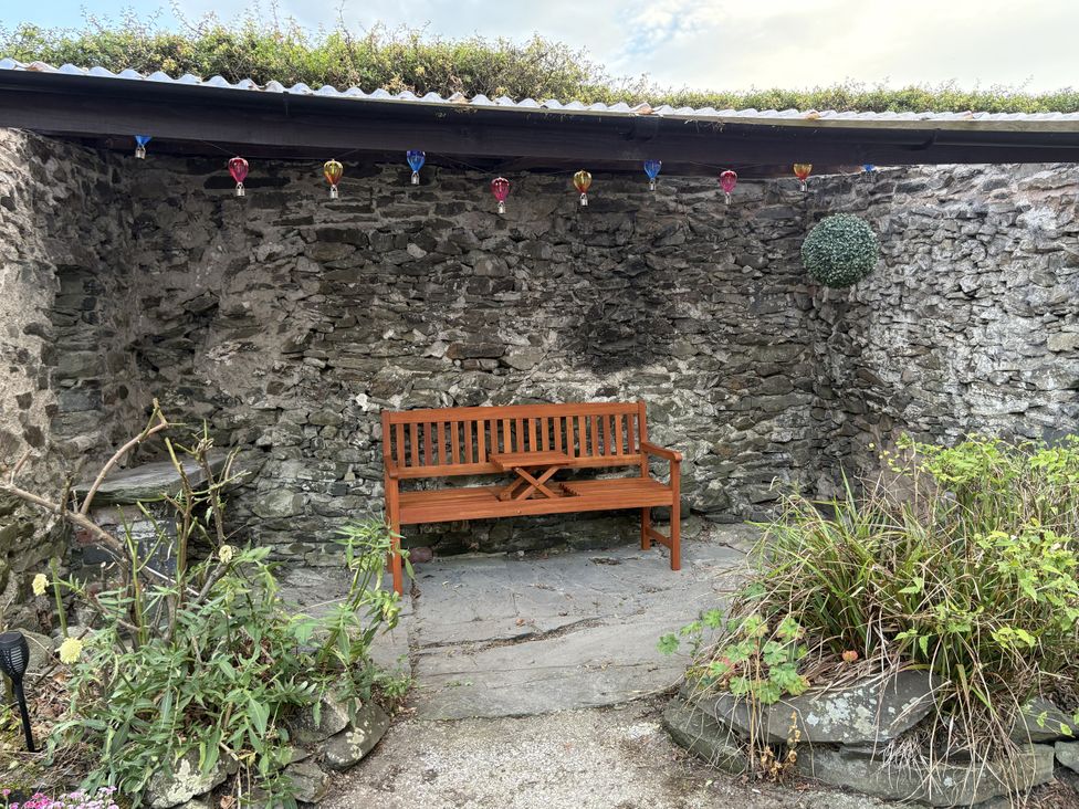 An outdoor seating area with a wooden bench and stone wall at Garth Cottage Groes near Denbigh