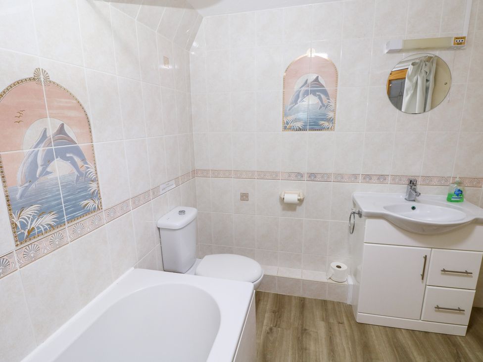 A bathroom with a bathtub, toilet, sink, and wall tiles at Cherry Trees in Haverfordwest