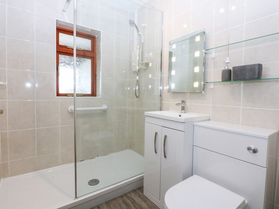 A bathroom with a shower, toilet, sink, and mirror at Eryl Nefyn