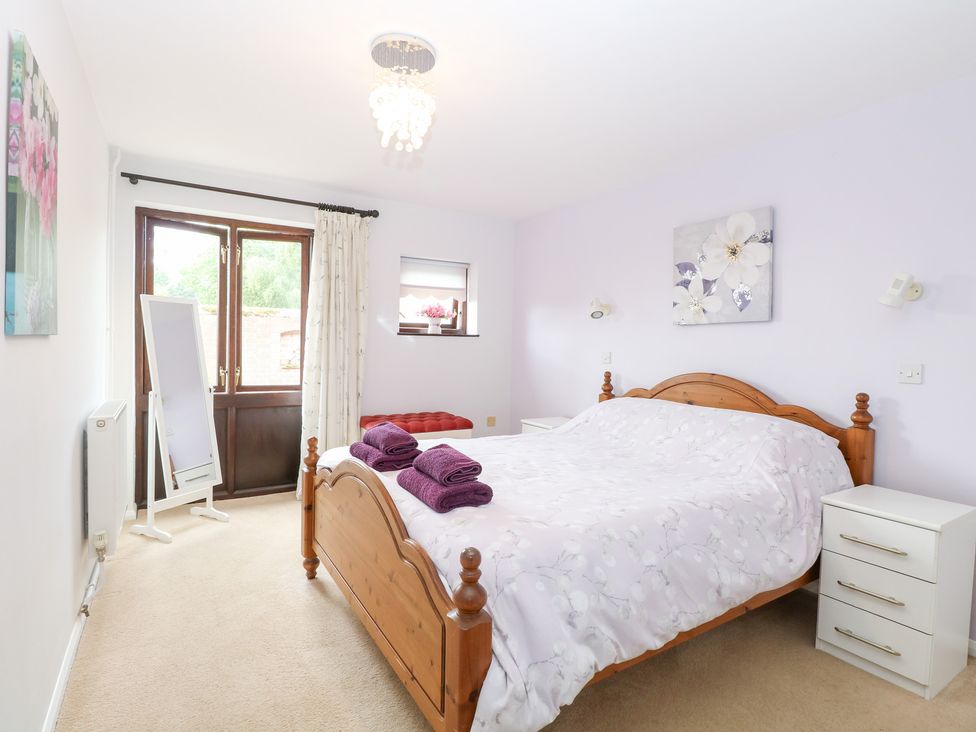 A bedroom with a wooden bed and a mirror at Lowbrook Cottage Dickleburgh near Diss