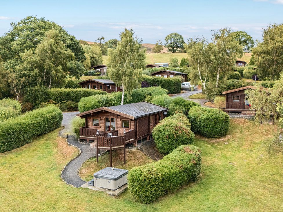 A view of log cabins surrounded by trees and bushes at Glanyrafon Bungalow St Harmon