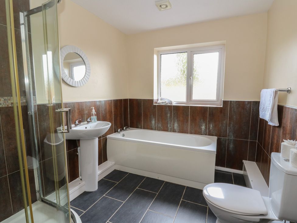 A bathroom with shower, bathtub, sink, and toilet at Glanyrafon Bungalow St Harmon