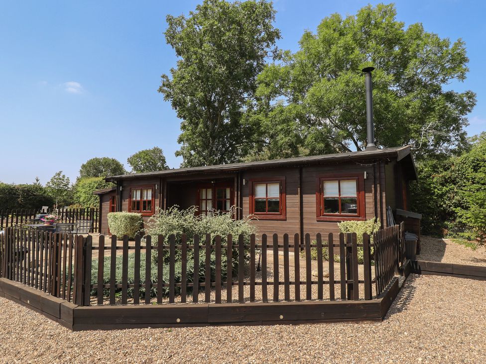 A log cabin with a fence and chimney at Tythe Lodge – Hot Tub Retreat in Rural Lincolnshire | Family-Friendly Lodge Near Heckington