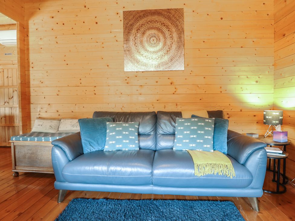 A living room with a blue sofa and wooden walls at Tythe Lodge – Hot Tub Retreat in Rural Lincolnshire | Family-Friendly Lodge Near Heckington