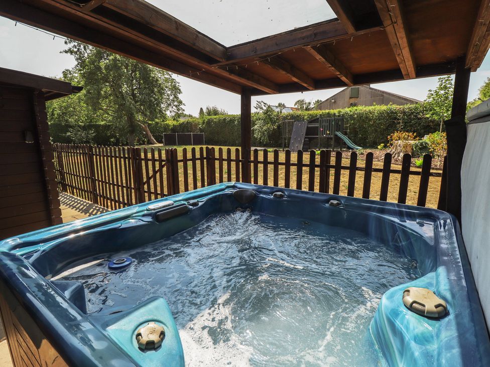 A hot tub with a wooden fence and grass area at Tythe Lodge – Hot Tub Retreat in Rural Lincolnshire | Family-Friendly Lodge Near Heckington