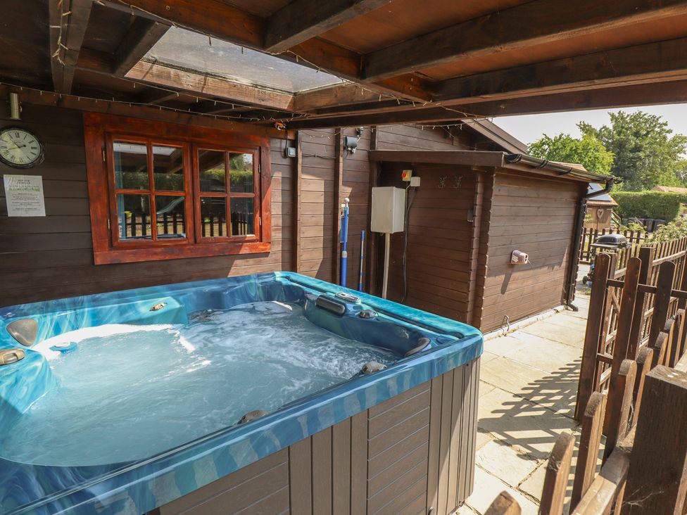 A hot tub next to a wooden cabin at Tythe Lodge – Hot Tub Retreat in Rural Lincolnshire | Family-Friendly Lodge Near Heckington