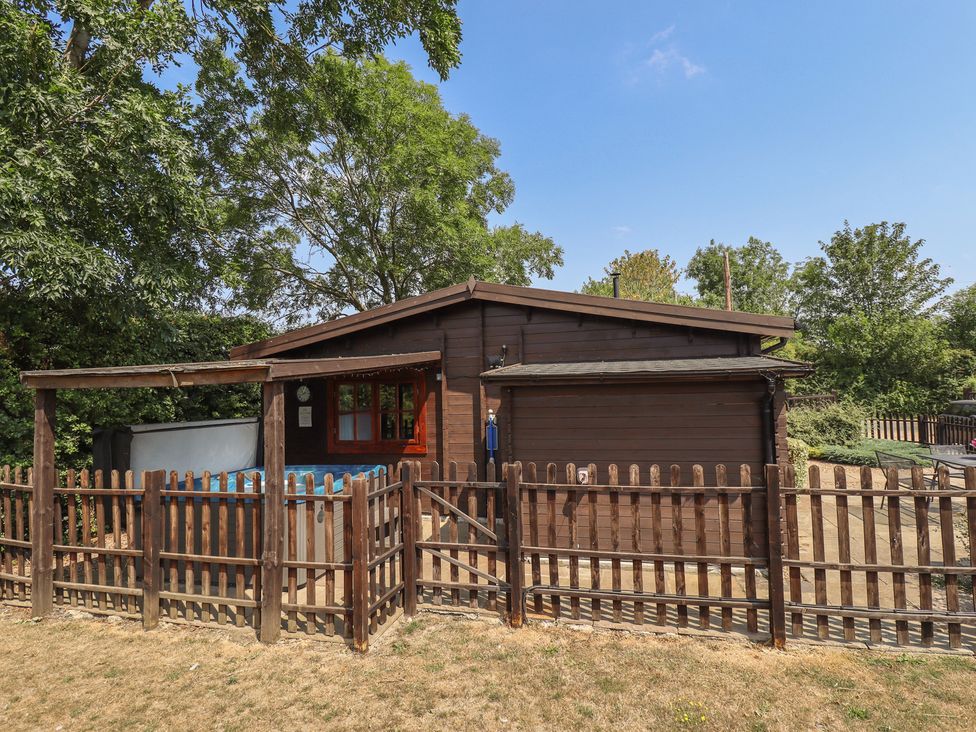 A wooden lodge with a fence and hot tub at Tythe Lodge – Hot Tub Retreat in Rural Lincolnshire | Family-Friendly Lodge Near Heckington
