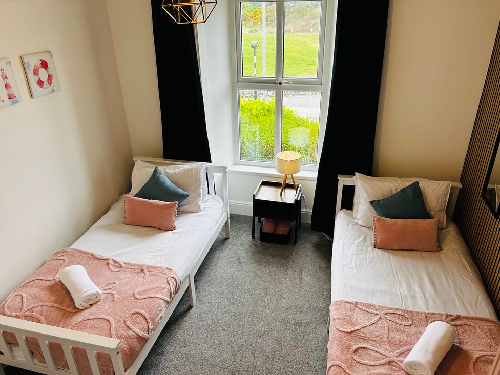 A bedroom with two beds, a lamp, and a window at Trearddur View in Treaddur Bay