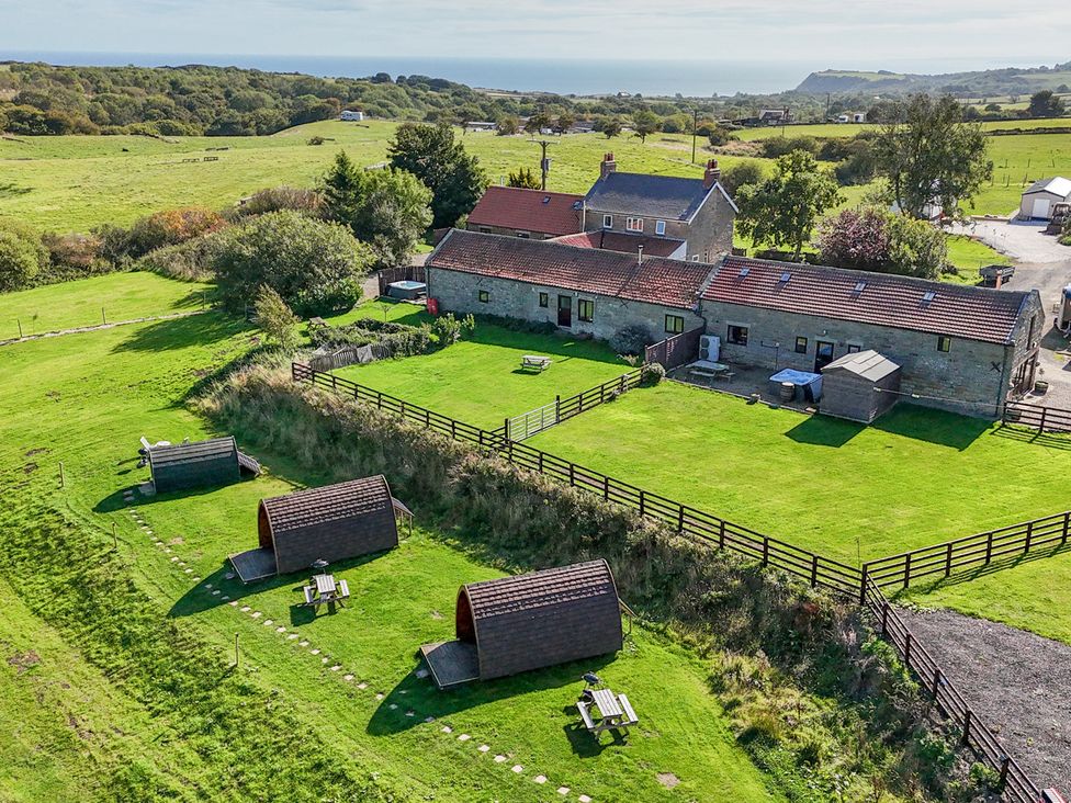 An outdoor area with a house, picnic tables, and wooden huts at Stable Cottage in Staintondale