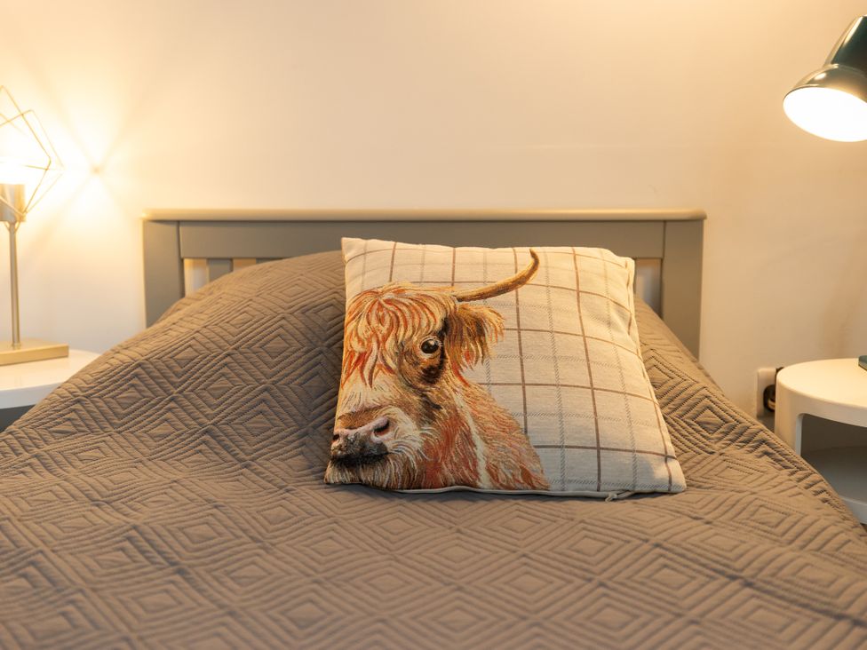 A bed with a pillow featuring a highland cow design at The Coach House in Llangollen