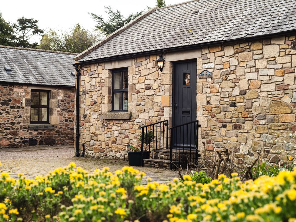A stone cottage with a door and flowers at Blueberry Cottage in Akeld near Wooler