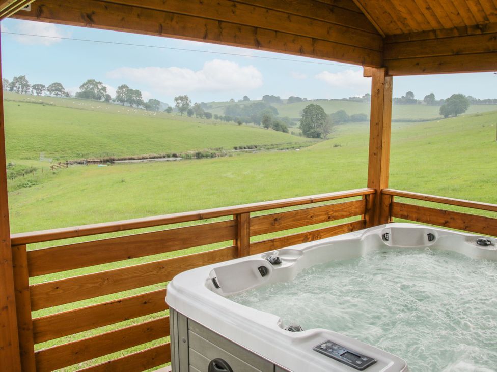 A hot tub on a wooden deck overlooking grass fields at Manor Farm Lodges - Dragon Lodge in Newtown