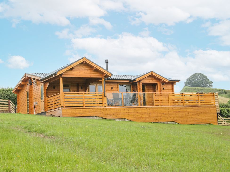 A wooden cabin with a deck in a grassy area at Manor Farm Lodges - Dragon Lodge Newtown
