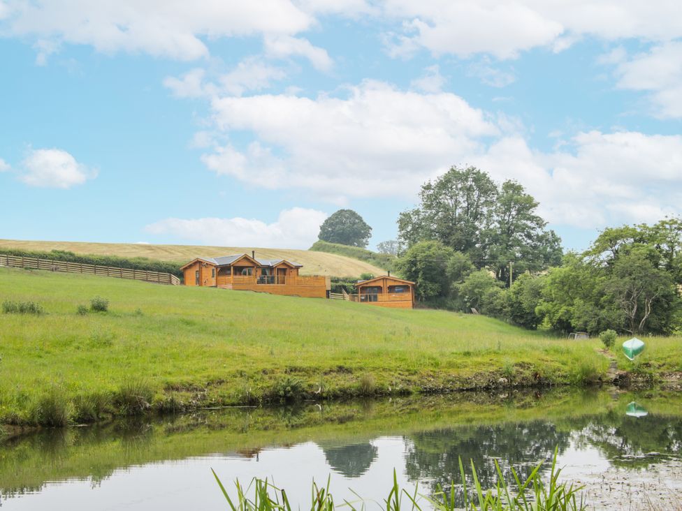 A view of wooden cabins by a pond at Manor Farm Lodges - Dragon Lodge in Newtown