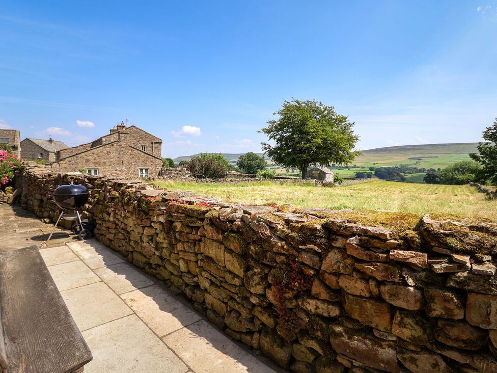 An outdoor area with a stone wall, barbecue, and view of houses and fields at Lyndhurst in Carlton-in-Coverdale, near Leyburn