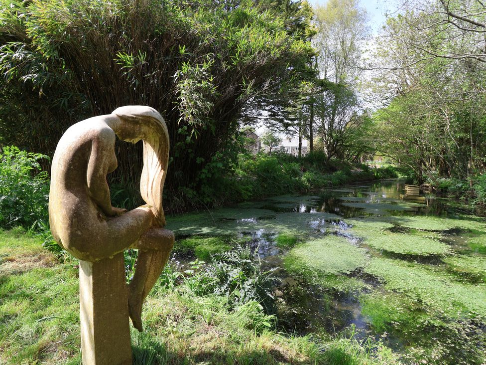 A sculpture beside a pond surrounded by plants at Lily Cottage in Looe