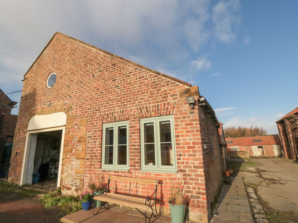 An exterior view of a brick building with a bench at The Old Milk House near Potto near Hutton Rudby