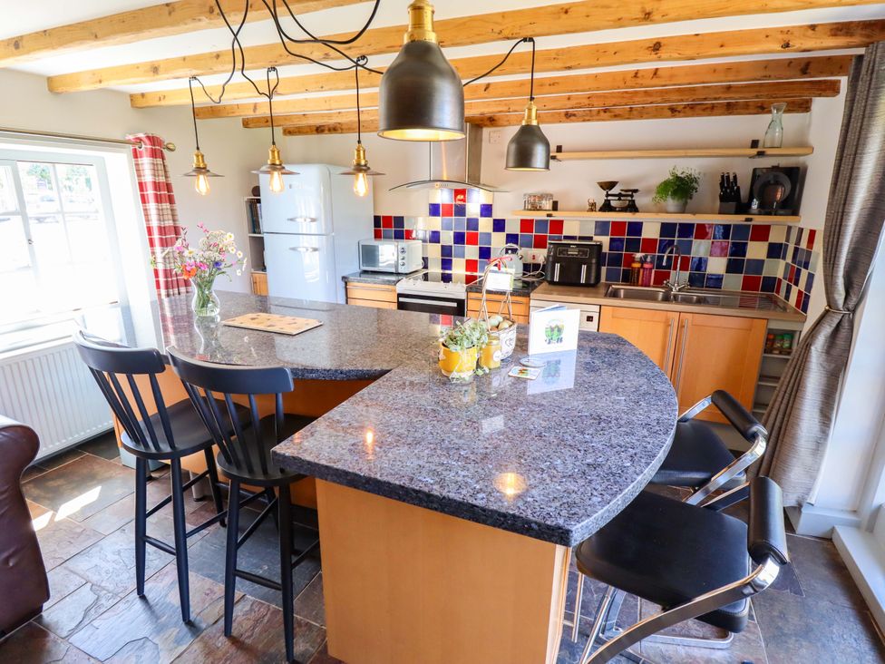 A kitchen with a countertop, bar stools, and appliances at Gables Cottage in Market Rasen