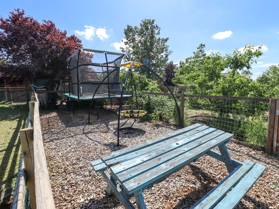 An outdoor play area with a trampoline and swing set at Gables Cottage, Market Rasen