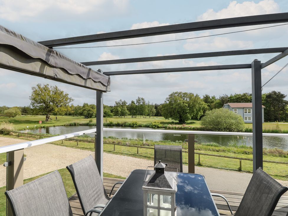 An outdoor area with a table and chairs overlooking a lake at Links View in Fritton