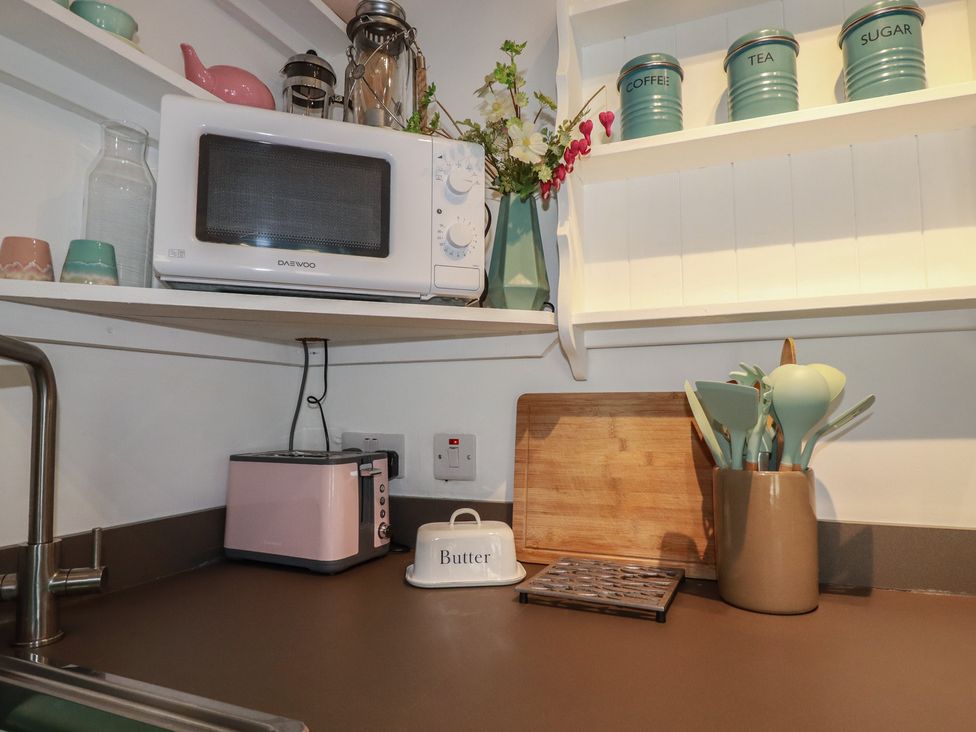 A kitchen with a microwave, toaster, and utensils container at Smugglers Cottage Trebarwith Strand near Tintagel