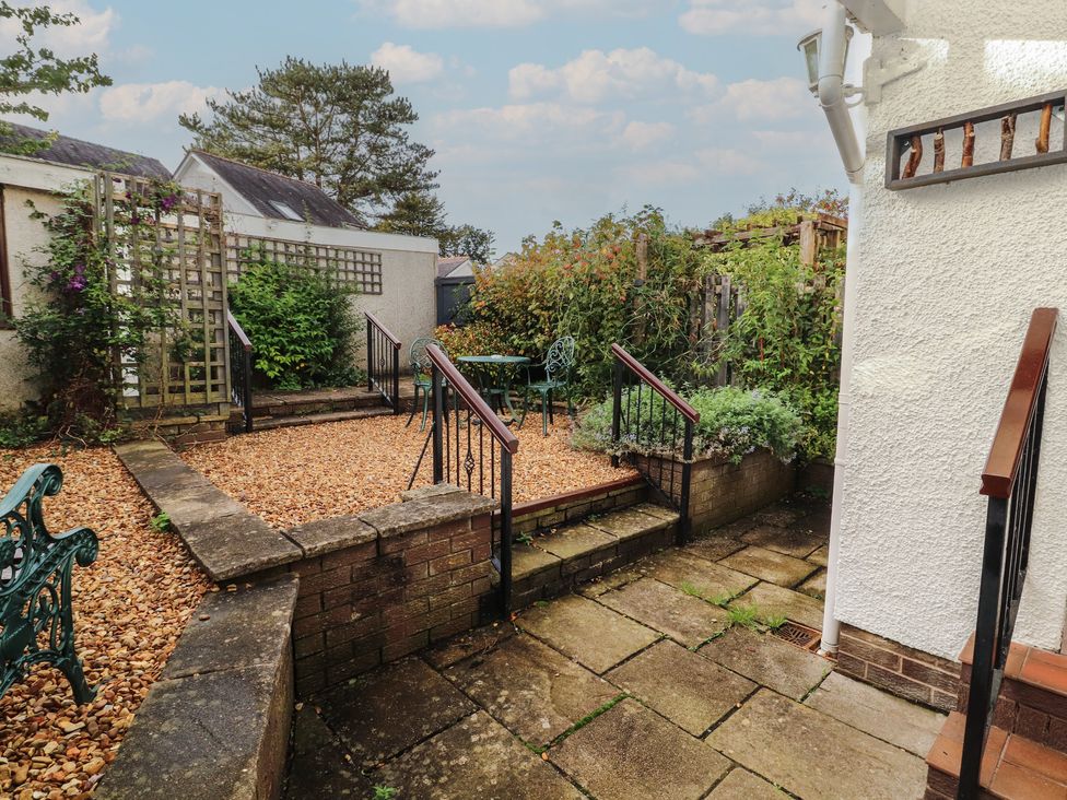 A garden area with gravel, steps, green furniture and plants at Riverside Cottage in Cockermouth