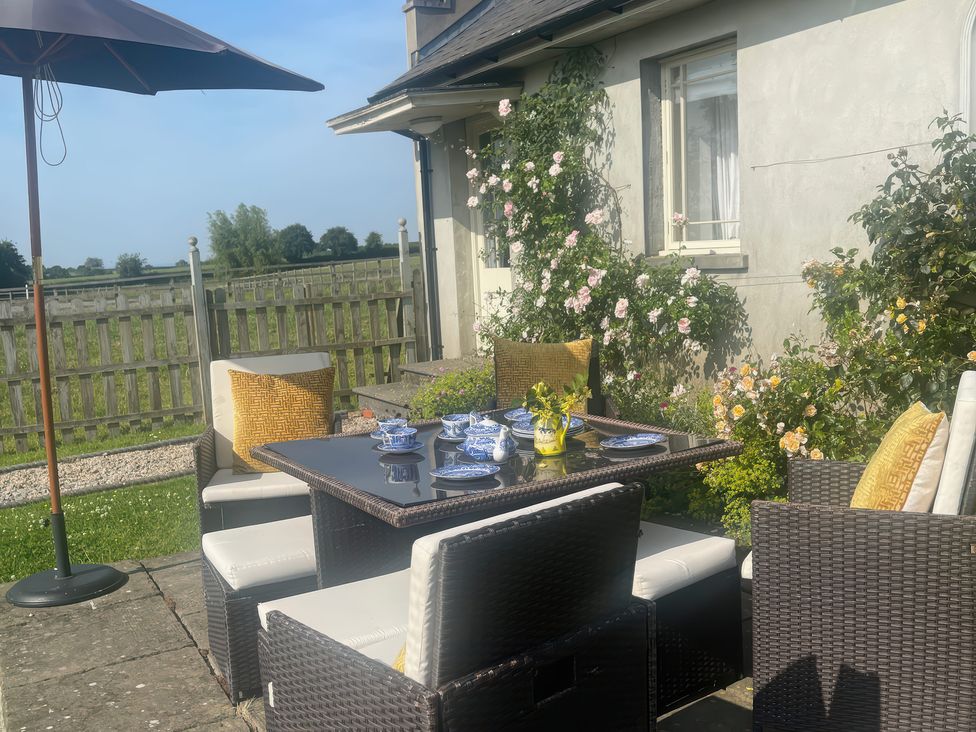 A garden dining setup with a table, chairs, and umbrella at Maple Cottage Buckland Newton near Dorchester