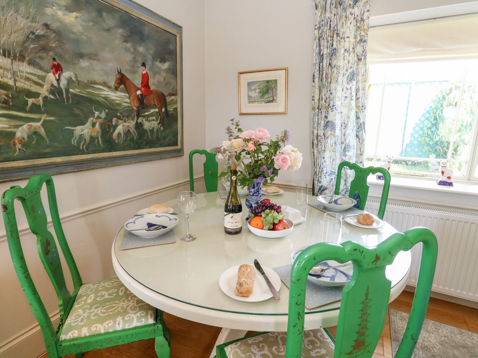 A dining room with a round table set with plates and a wine bottle at Maple Cottage Buckland Newton near Dorchester