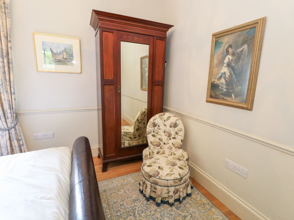 A bedroom with a wardrobe and floral chair at Maple Cottage in Buckland Newton near Dorchester