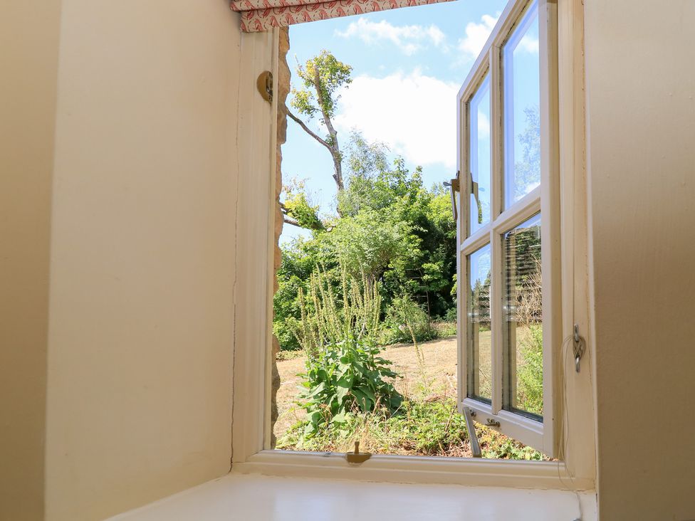 A view of plants and grass through an open window at Upper Mill Barn, Coln St Aldwyns, near Bibury