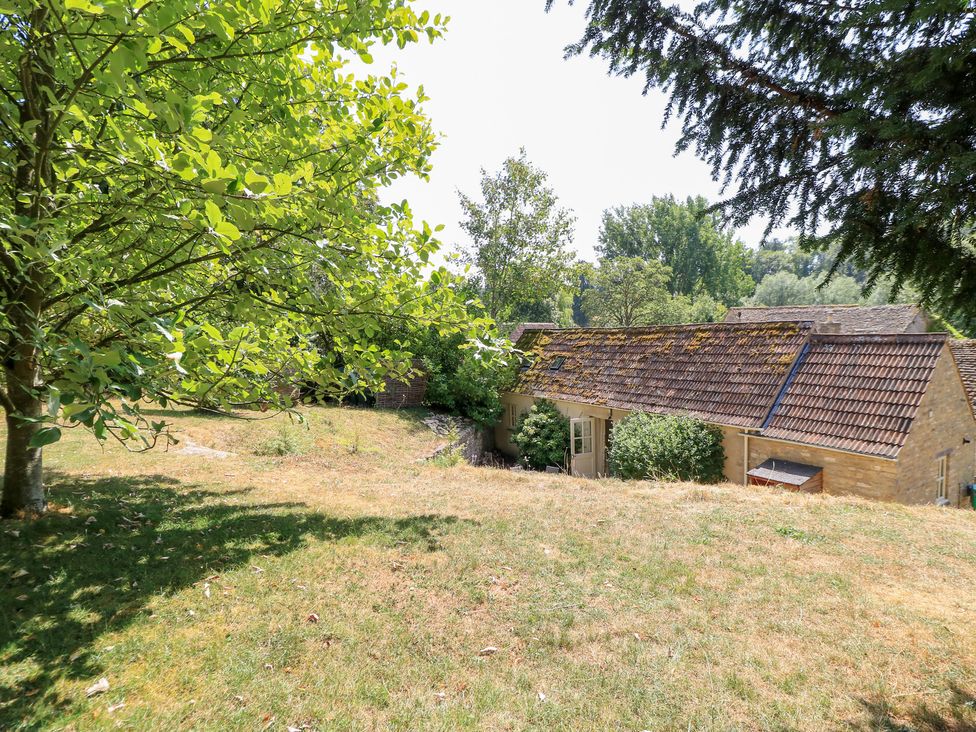 A garden with trees and a building at Upper Mill Barn in Coln St Aldwyns near Bibury