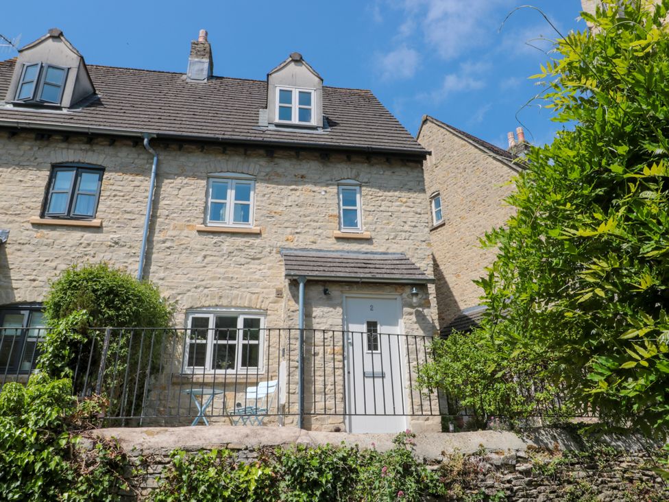 Exterior of a stone house with white door and windows and a small patio with table and chairs at Batemans in Nailsworth